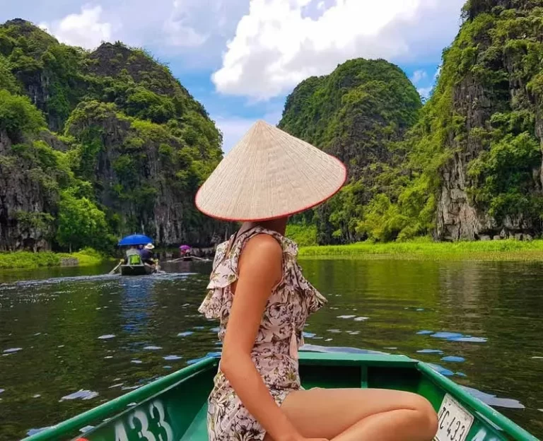 1-tourist-in-a-conical-hat-sitting-on-a-boat-navigating-through-the-scenic-limestone-karsts-and-lush-landscapes-of-trang-an