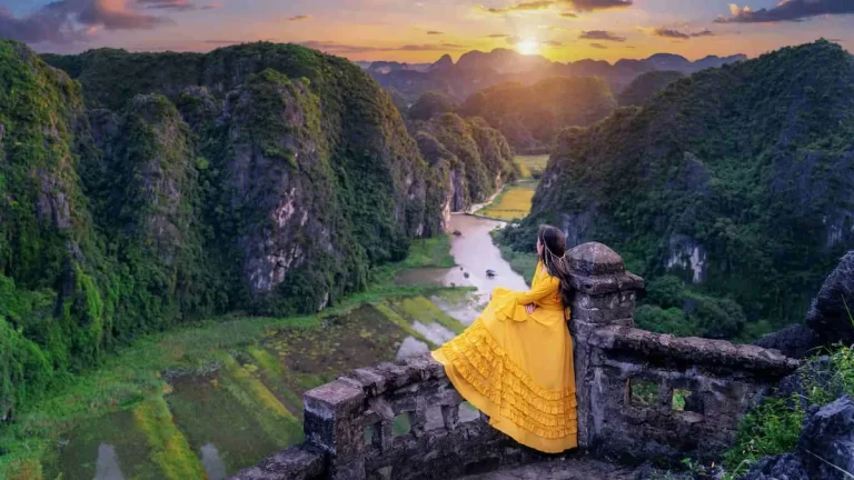1-woman-in-a-yellow-dress-enjoying-the-view-from-a-stone-lookout-at-mua-cave-with-a-valley-below